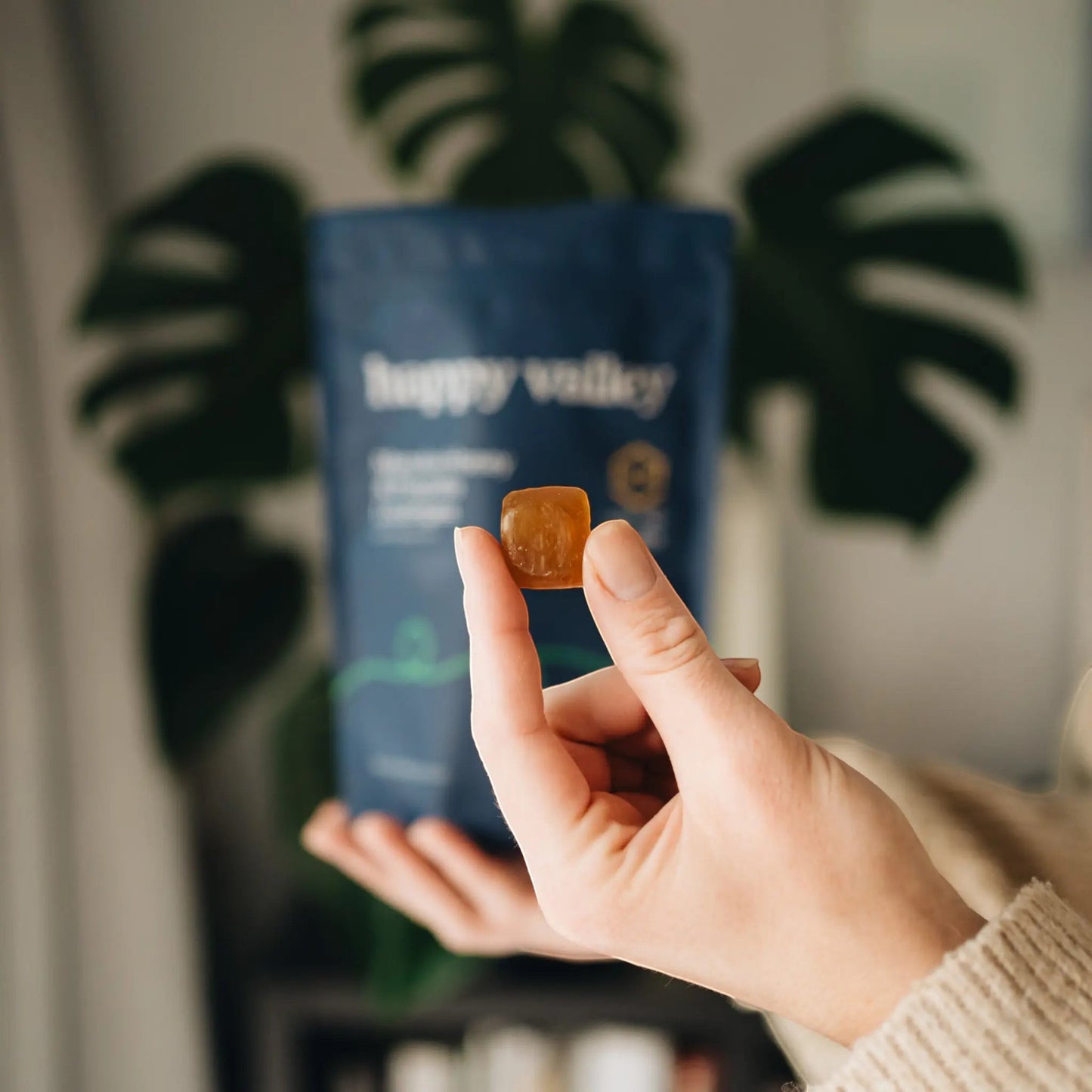 Happy Valley Honey Manuka Honey & Propolis lozenge held by fingers, with pouch in background.